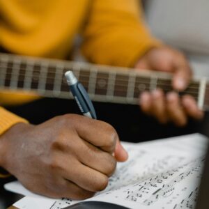 Close-up of a person writing on sheet music while holding a guitar, focusing on creativity and musical composition.